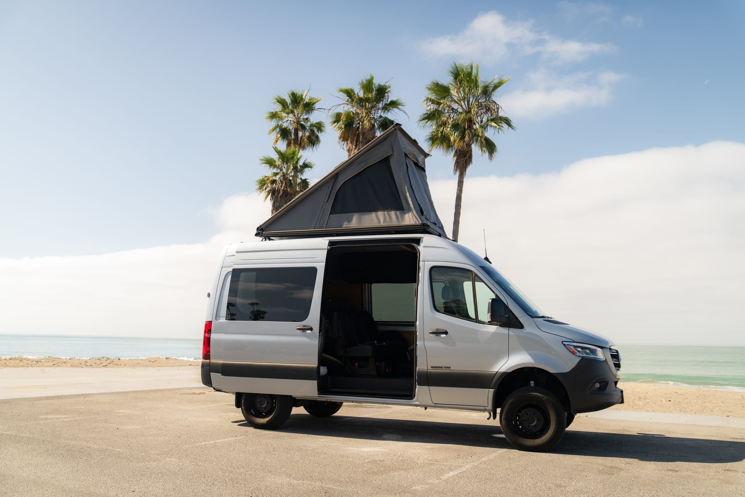 Camper van with pop-top roof raised parked at the beach beneath tall palm trees