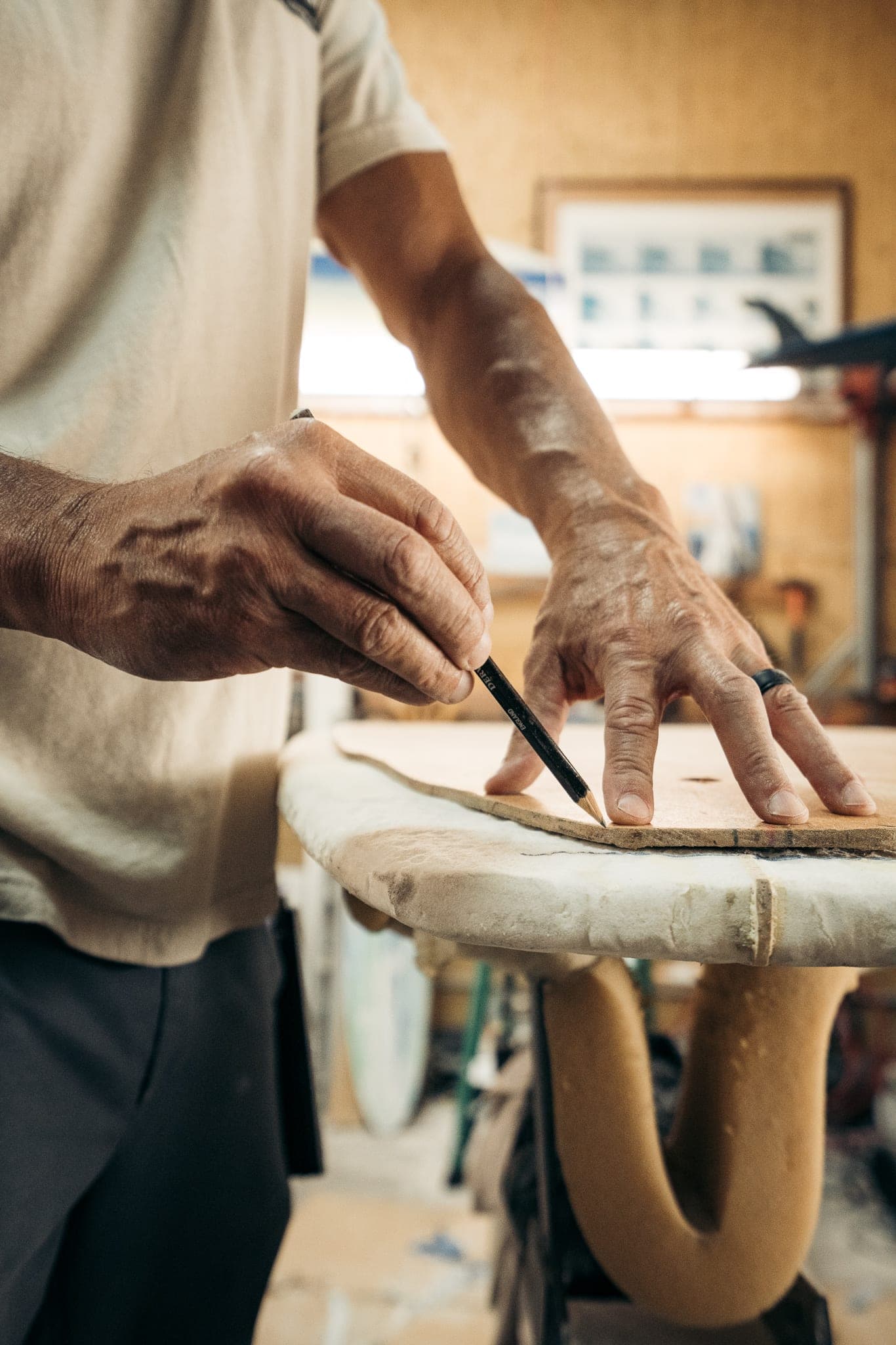 Surfboard shaper tracing a template onto a foam blank with a pencil in his workshop