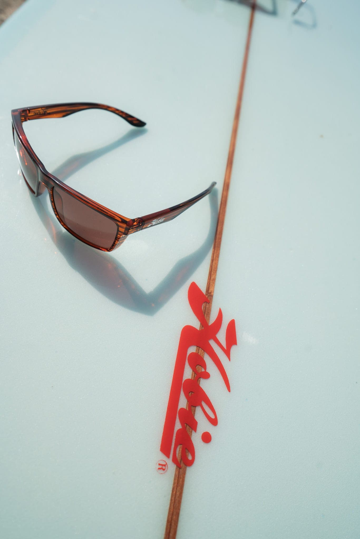 Tortoiseshell sunglasses casting a shadow on a pale blue Hobie longboard with a wooden stringer