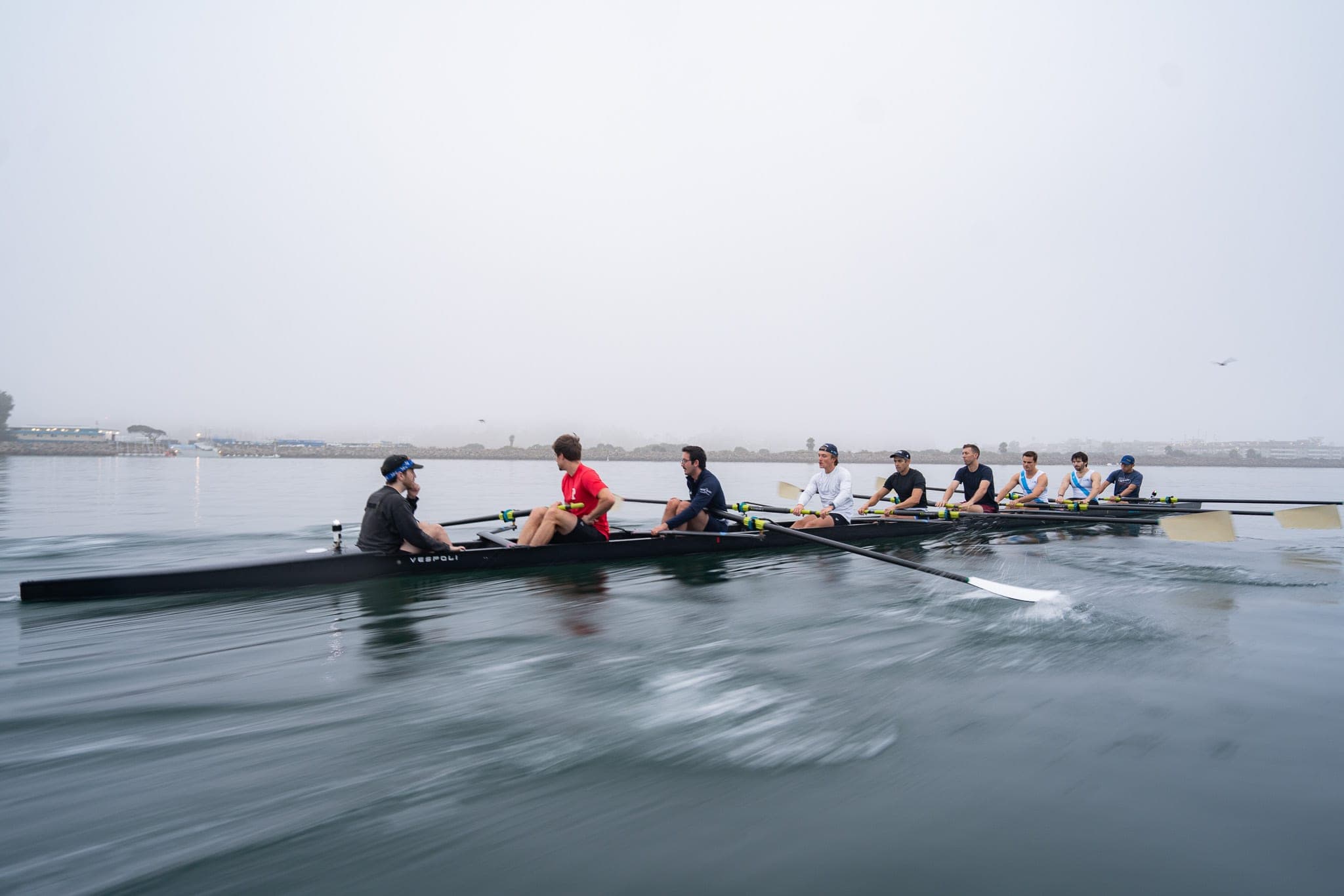 Men's rowing eight gliding across calm foggy harbor water
