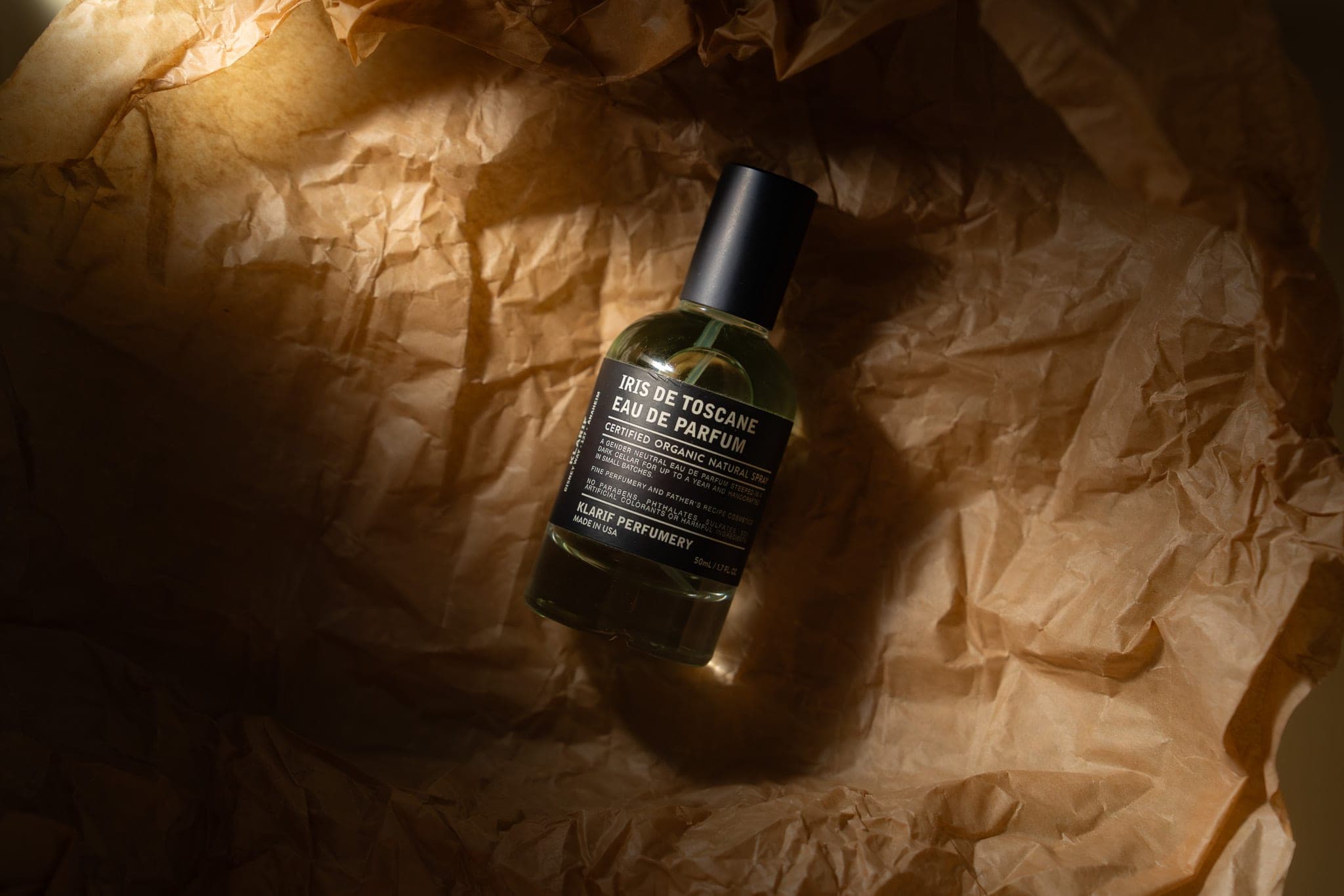 Bottle of Iris de Toscane eau de parfum nestled in crumpled kraft paper under warm directional light