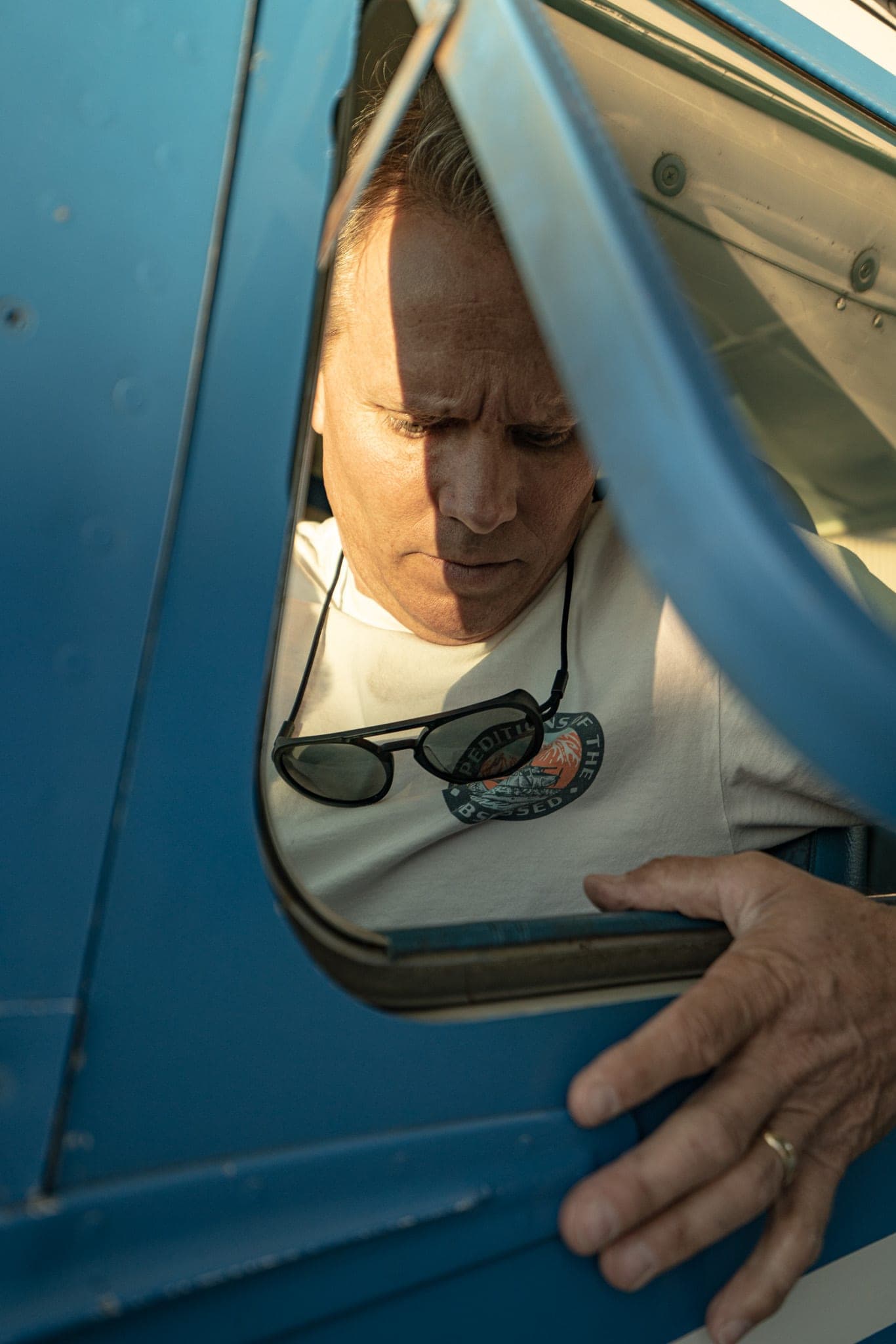 Man framed in the open window of a blue vintage airplane, lit by low sun