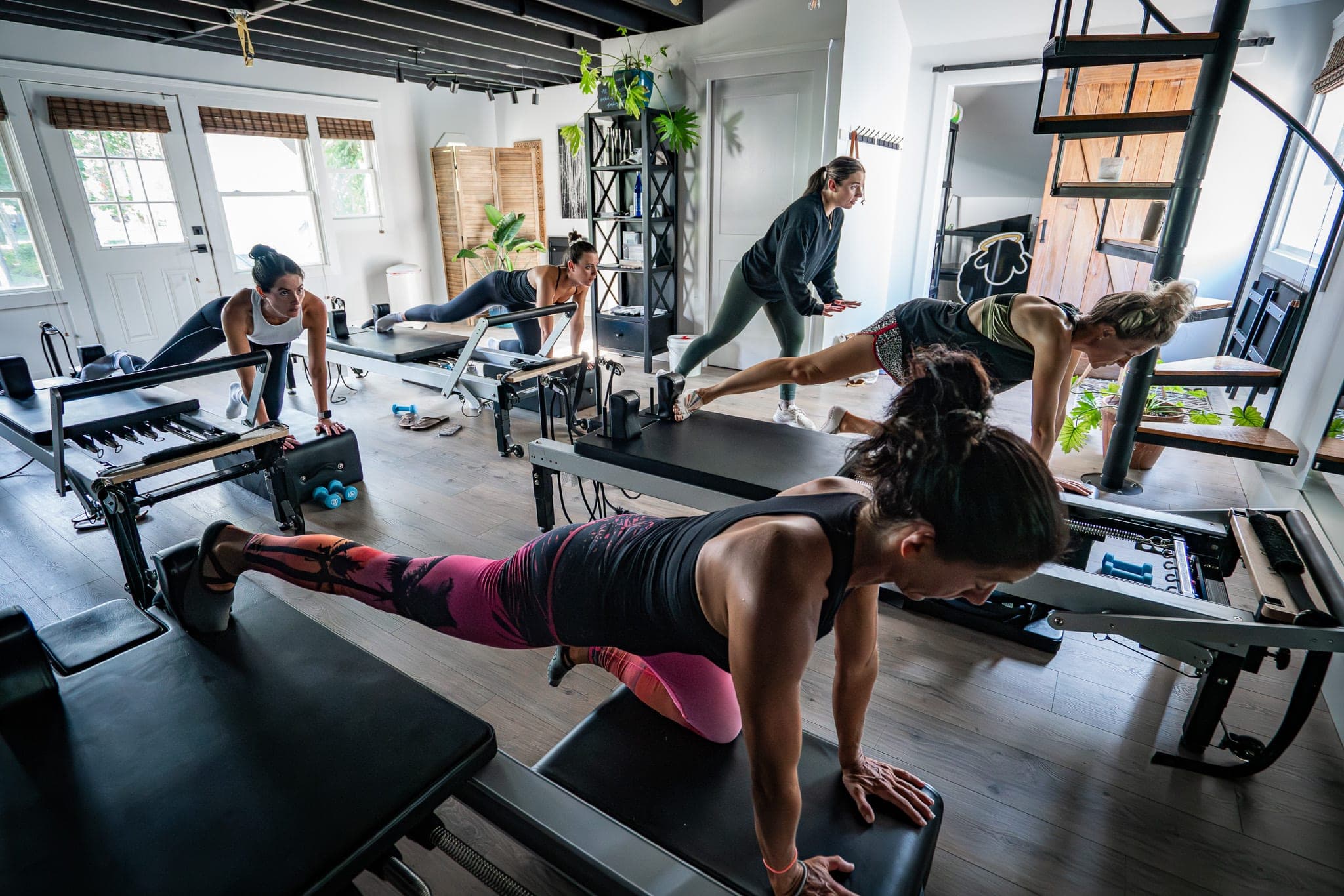 Group Pilates reformer class in a bright plant-filled studio with a spiral staircase