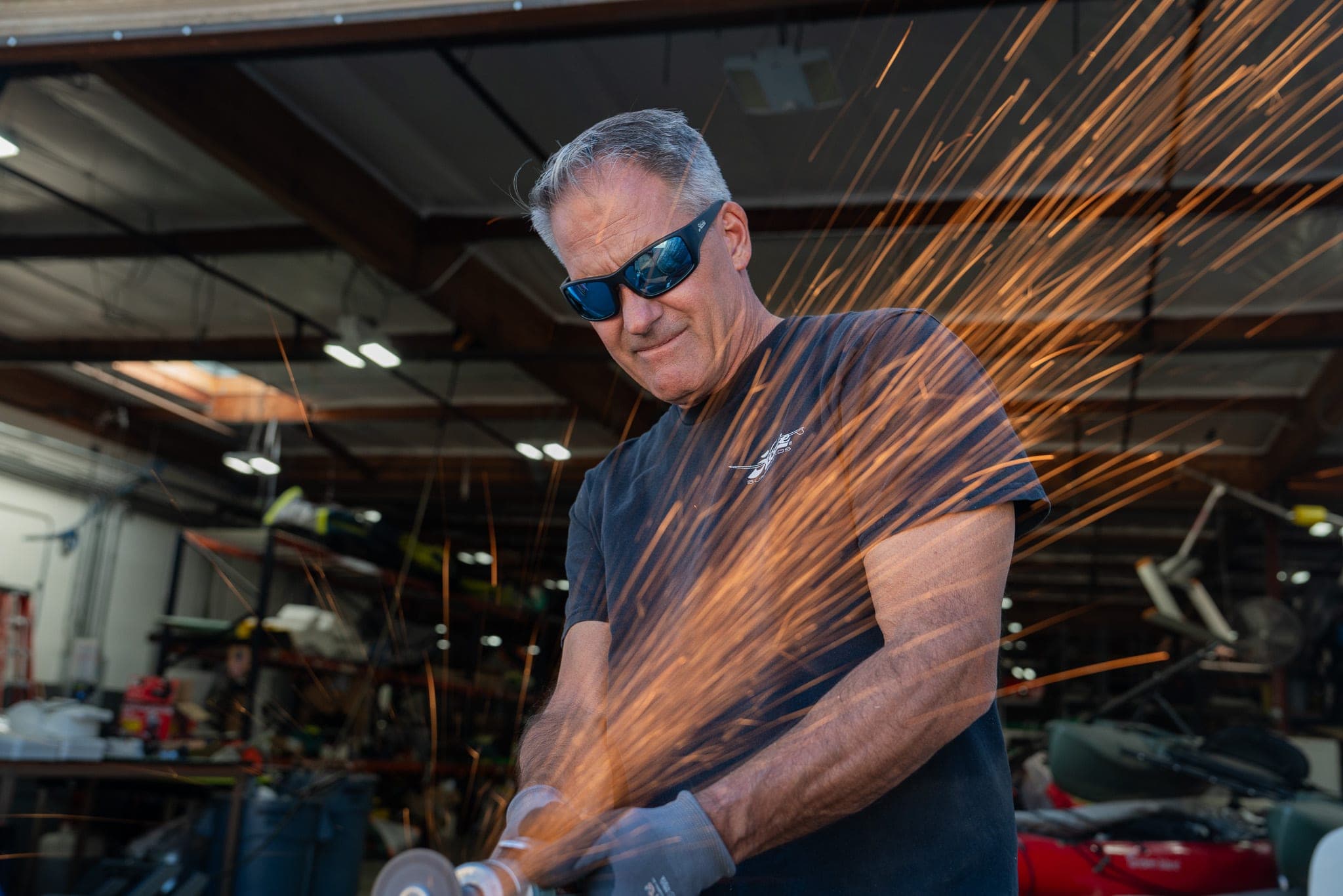 Craftsman in sunglasses grinding metal in a workshop as orange sparks streak across the frame
