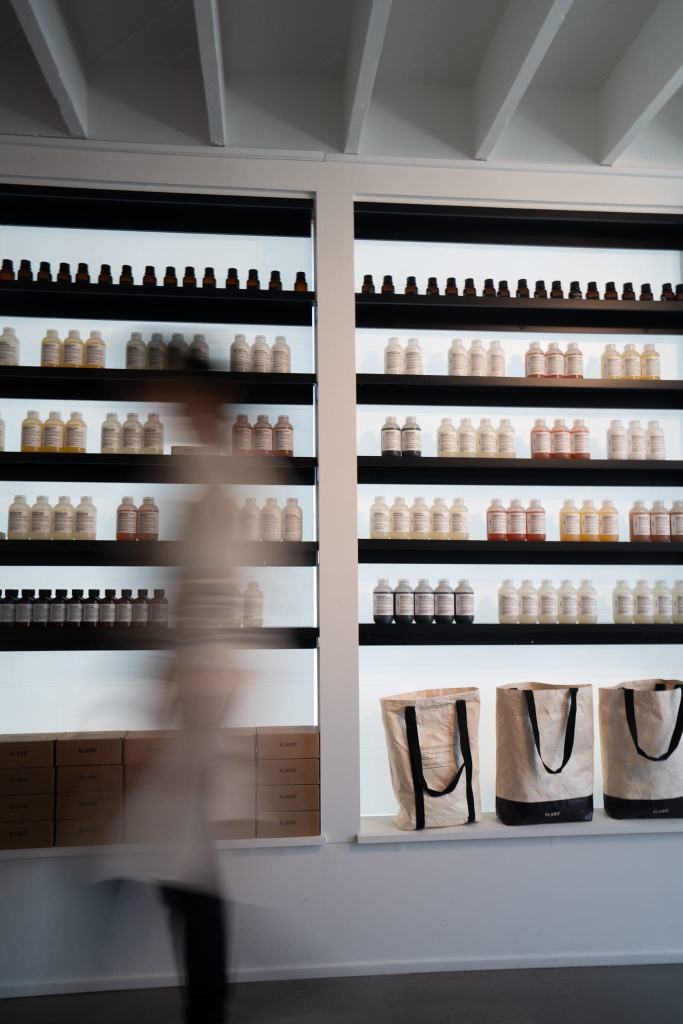 Motion-blurred figure walking past backlit shelves of apothecary bottles in a minimalist shop